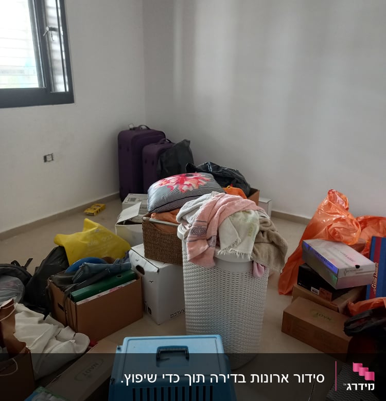 חדר עם קופסאות, מזוודות וסל כביסה מלא בבגדים.